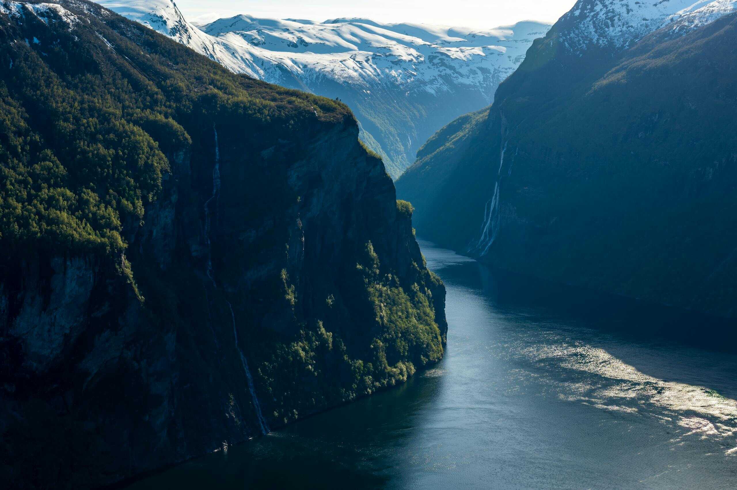 Breathtaking view of Geiranger Fjord, Norway, with snow-capped mountains and serene blue waters.
