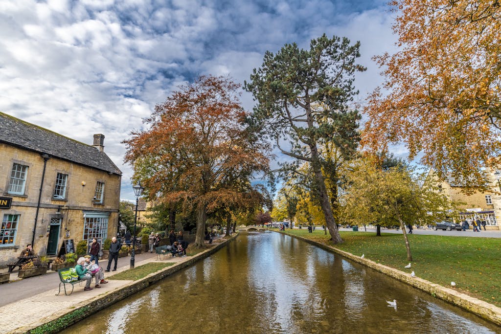 Charming autumn view of Bourton-on-the-Water with a tranquil stream and vibrant foliage.